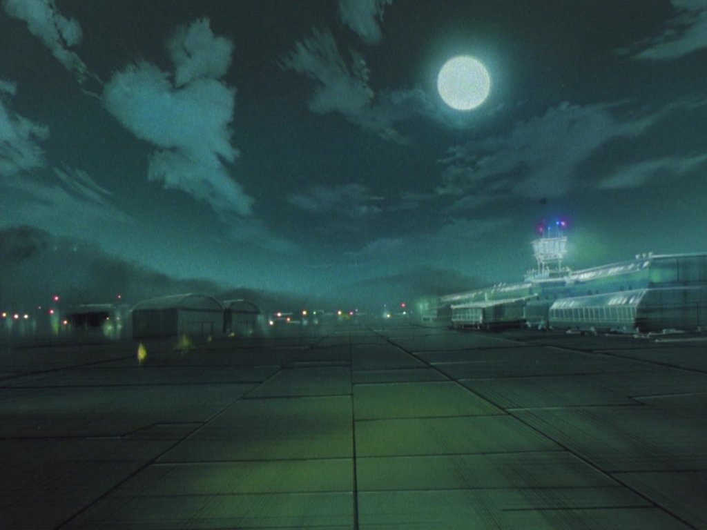 Vista noturna de um aeroporto com hangar e torre de controle iluminados sob a lua cheia.