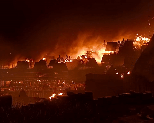 Uma vila em chamas à noite, com fumaça e chamas iluminando o céu escuro.