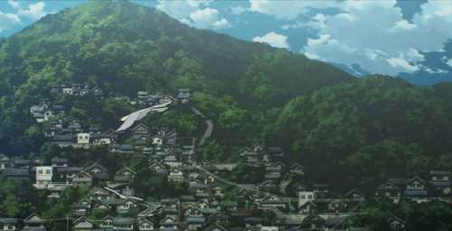 Vista panorâmica de uma cidade montanhosa com casas empilhadas, cercada por vegetação verde e um céu azul com nuvens brancas.