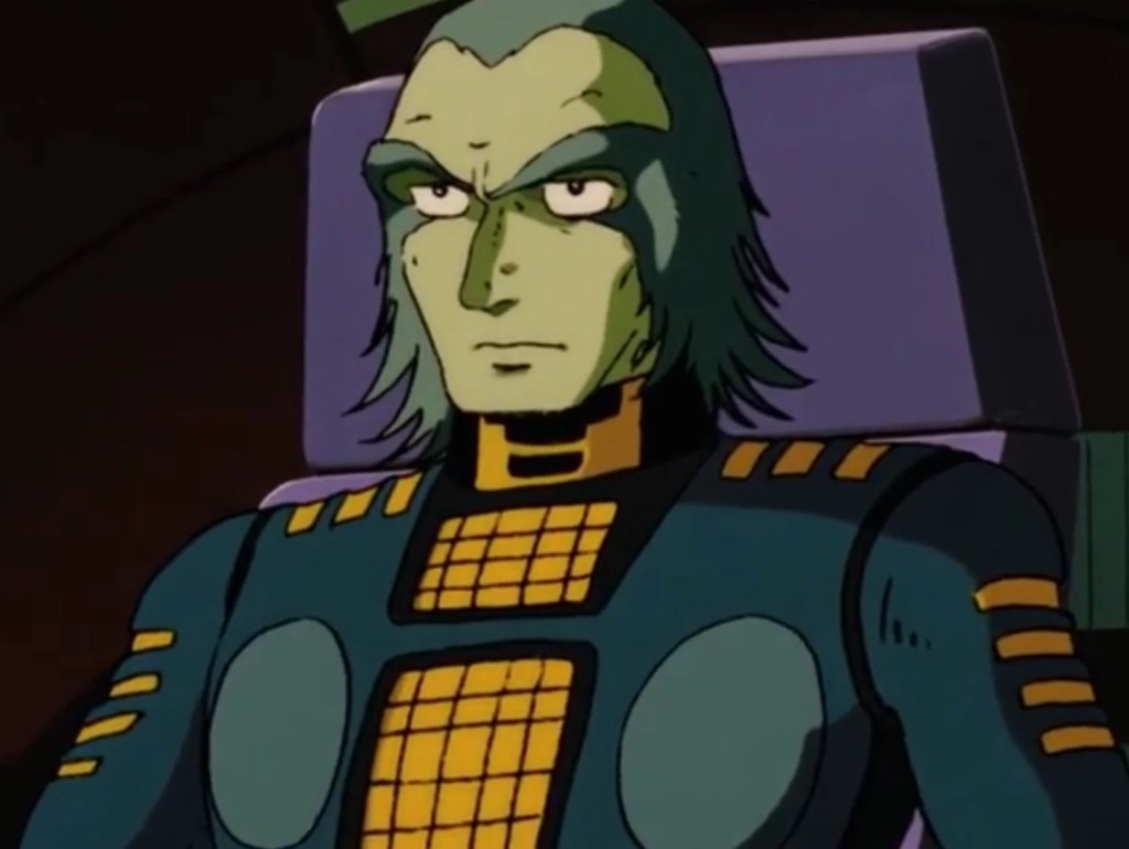 Personagem animado com cabelo verde e pele esverdeada, usando um traje de combate com detalhes em amarelo e azul, sentado em um assento.